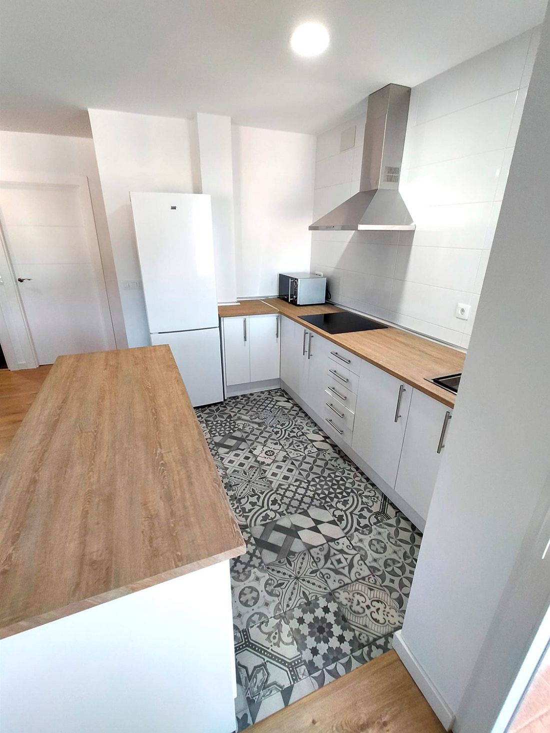 Cocina reformada con muebles blancos y madera de tono claro y suelo cerámico con dibujo geométrico