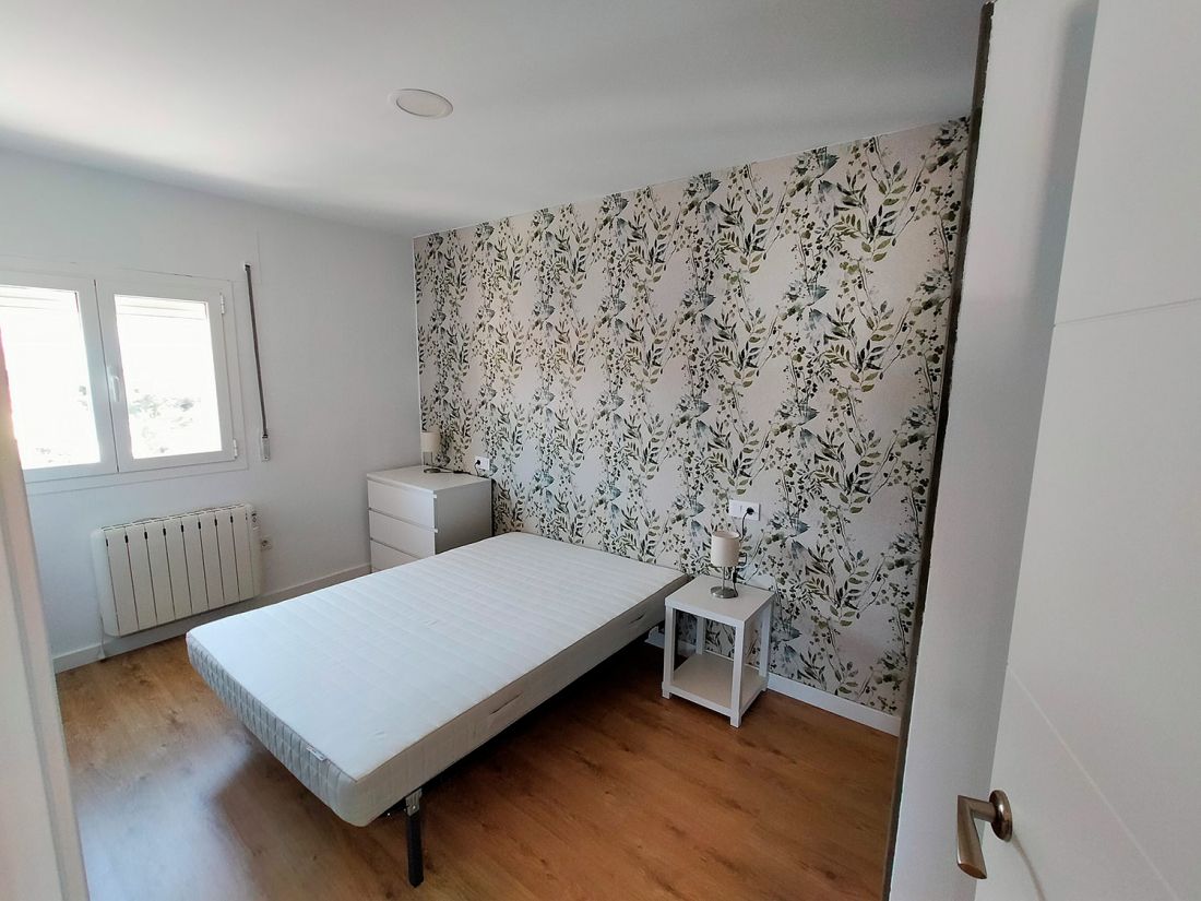 Dormitorio con muebles y carpintería en color blanco y pared frontal empapelada con tema vegetal