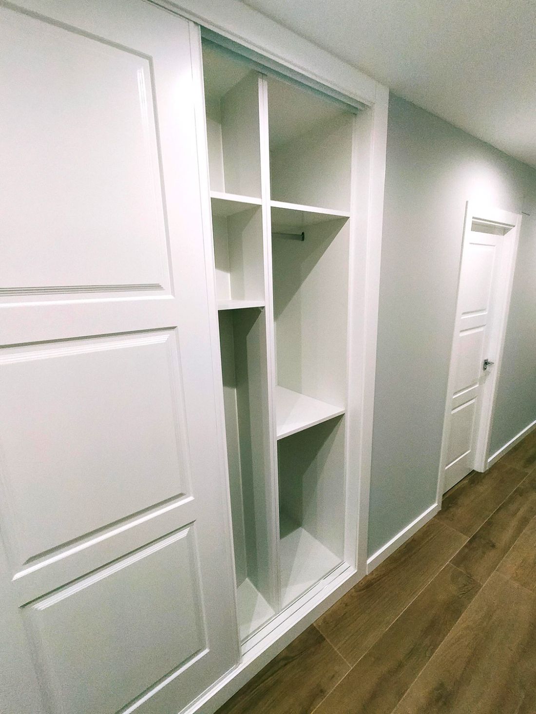 Pasillo de casa reformada con tarima de madera y paredes y armarios en color blanco