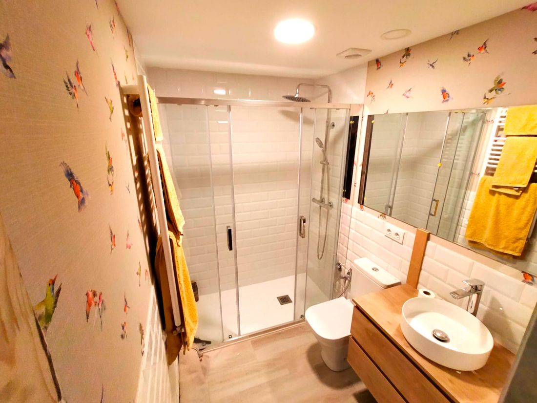 Baño reformado con muebles de madera en tono claro y pared empapelada con motivo de pájaros